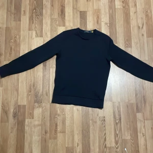 Mörkblå sweatshirt från Polo Ralph Lauren - En stilren mörkblå sweatshirt från Polo Ralph Lauren med diskret logotyp i relief på bröstet. Tröjan har rund halsringning och långa ärmar, perfekt för en clean och klassisk. Väldigt prisvärd med tanke på skicket.