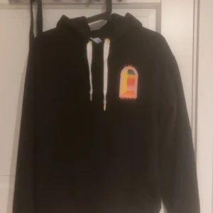 Svart hoodie Casablanca med färgglatt tryck - Svart hoodie från Casablanca med stor färgglad gradient-arch logga på ryggen och mindre tryck på bröstet. Tröjan har huva med vita snören och guldiga detaljer. Perfekt för dig som gillar streetwear och snygga loggor. Kom med prisförslag!