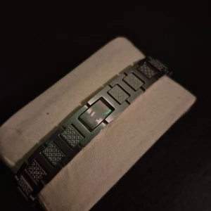 Silverfärgat armband från Lacoste - Stilrent armband i silverfärgad metall från Lacoste 21cm lång med rektangulära länkar och diskret rutmönster på varje länk. Klassisk Lacoste-logga ingraverad på spännet. Perfekt för dig som gillar minimalistisk design med en sportig touch.