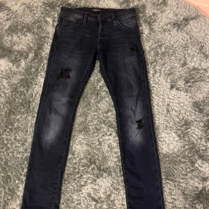 Jack&jones jeans - Snygga mörkblå skinny jeans från Jack&Jones med slitna detaljer på benen. Klassisk femficksmodell med normal midja och stretchigt jeanstyg som sitter tajt hela vägen ner. Perfekta för dig som gillar en trendig och avslappnad look.