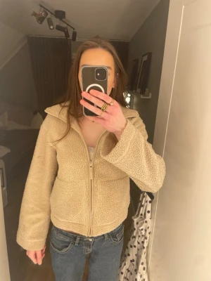 Beige teddyjacka med dragkedja - Mysig beige teddyjacka med krage och hel dragkedja framtill. Jackan har en avslappnad passform och är tillverkad i fluffigt teddy-material som håller dig varm. Perfekt för lager-på-lager och en chill vardagslook.