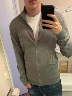 Grå full zip - Säljer denna stilrena full zip tröjan i färgen grå. Tröjan är bekväm och tunn och har en riktigt schysst passform, perfekt nu när våren börjar närma sig! Slim fit modell i storlek M så den passar bra på kroppen. Tveka inte på att skriva om du har några fler frågor eller funderingar💯