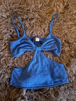 Blå ribbad linnetopp med cut-out - Trendig blå linnetopp  med ribbad struktur, smala axelband och snygg cut-out framtill. Toppen har en twistad detalj vid bysten och är croppad, perfekt för sommarens alla tillfällen.