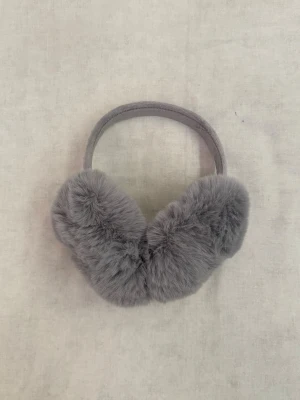 Grå fluffiga öronmuffar - Aldrig använd. Supermjuka och fluffiga öronmuffar i grått med fuskpäls. Perfekta för att hålla öronen varma under kalla dagar. Bågen är också klädd i mjukt tyg för extra komfort. En snygg accessoar för vintern!