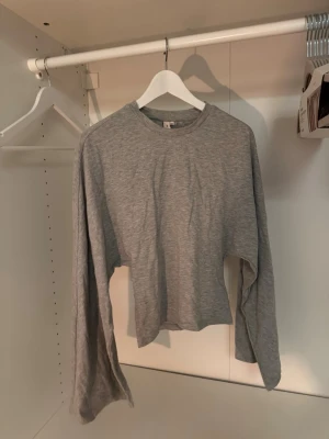 Grå croppad långärmad tröja - Säljer en enkel och stilren grå croppad långärmad tröja i mjukt bomullsmaterial. Tröjan har rund halsringning, vida ärmar och tajt i midjan. Perfekt att matcha med höga jeans eller kjol. Drömmig topp men har en likadan i en annan färg som jag tycker passar mig bättre så hoppas att denna kan komma till användning hos någon annan🙏🏼🤍