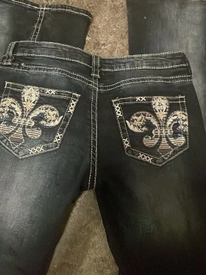Mörkblå Lågmidjade jeans - Snygga mörkblå Lågmidjade jeans med kontrasterande vita sömmar och stora broderade mönster på bakfickorna. Jeansen har klassisk femficksdesign och en cool, tvättad look. Perfekta för dig som vill sticka ut med detaljer.