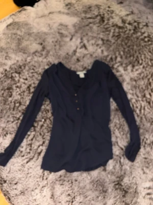 Mörkblå långärmad topp - En stilren mörkblå långärmad topp med v-ringning och knappar framtill. Perfekt att matcha med jeans eller kjol för en enkel och snygg look.