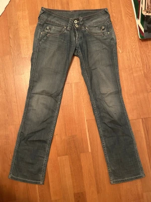 Lowwaist Pepe Jeans med broderade fickor - Snygga blå jeans från Pepe Jeans med raka ben och broderade bakfickor. Jeansen har klassisk femficksdesign, dubbla knappar i midjan och detaljerade sömmar. 