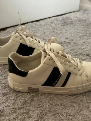 Vita Armani Exchange sneakers - Snygga vita sneakers från Armani Exchange med svarta detaljer och logga på sidan. Skorna har klassisk snörning med lite defekter inne i skorna vid hälarna, annars i gott skick