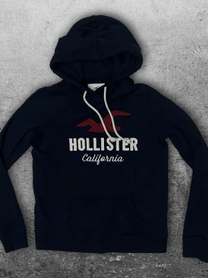 Hollister hoodie S - En fet hoodie från hollister i storlek S. Färg mörkblå med röd/vit tryck. Bra skick! 😀