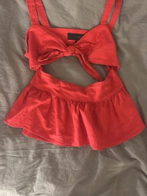 Röd knyt topp från Zara - Snygg röd topp från Zara med breda axelband och stor knytning framtill. Toppen har en volang nedtill och öppen detalj under bysten. Perfekt för sommarens alla tillfällen och ger en trendig look.