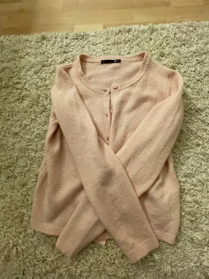 Ljusrosa kofta från lager 157 - Söt ljusrosa kofta från lager 157 med rund halsringning och knappar framtill. Koftan har långa ärmar och är stickad i ett mjukt material, perfekt för lager på lager. Enkel och stilren design som passar till det mesta.