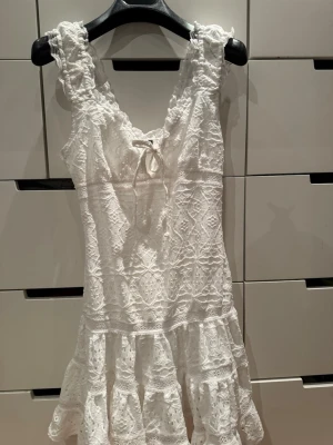 Vit spetsklänning med volang - Supersöt vit klänning i spets med volangkant och knytning fram. Perfekt för student eller midsommar! Bara använd en gång🥰