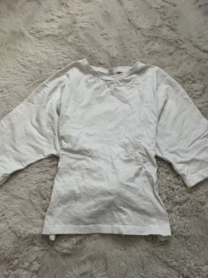 Vit knyt tröja  - Säljer en vit croppad topp från Nelly med rund hals och korta ärmar. Toppen har en öppen rygg med snyggt knytband som ger en cool detalj. Perfekt till jeans eller kjol för en chill look. Materialet är mjuk bomull🫶🏼