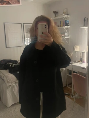 Svart overshirt med knappar - Stilren svart kappa med klassisk krage och stora knappar framtill. Modellen är rak och något oversized, vilket ger en avslappnad look. Perfekt för höst och vinter. Kappan har långa ärmar och två fickor framtill. Från H&M i storlek S