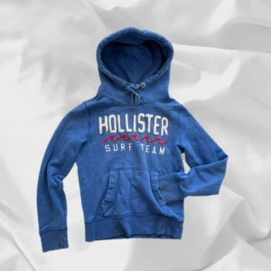 Hollister Hoodie - Fet hoodie från Hollister i Baby Blue – enkel att matcha och skön att bära. Ett stilrent val, noggrant utvalt med omsorg av narnen closet.  📩 Frågor? Hör gärna av dig! 📲 Följ oss här på Plick för fler uppdateringar. ♻️ Tack för att du handlar mer hållbart med barnen closet!