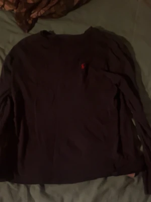 Mörkblå långärmad tröja från Polo Ralph Lauren - Klassisk mörkblå långärmad tröja från Polo Ralph Lauren med den ikoniska röda broderade loggan på bröstet. Tröjan har rund halsringning och är tillverkad i mjuk bomull som passar perfekt till alla tillfällen.