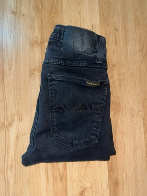 Nudie jeans  - Svarta snygga jeans från nudie jeans i skinny passform. Midja 28cm, längd 105cm. JAG SKICKAR EJ FLER BILDER NÄR JAG BÄR JEANSEN! för bättre inblick i passformen rekommenderar jag att googla på modellnamnet. För storleksguide kolla måtten noggrant då jeansen alltid kan vara uppsydda heller krympta och jag ej tar emot returer :) s6,3