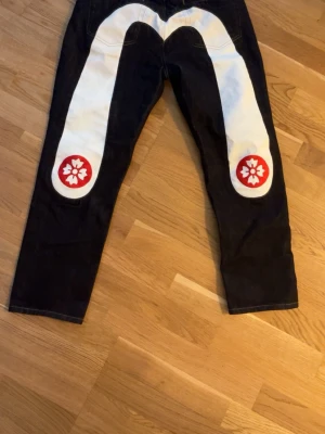 Evisu daicock jeans - Unika svarta jeans från Kapital med stor vit dekor på baksidan och röda blommor vid bensluten. Klassisk femficksmodell med raka ben och knappgylf. Perfekta för dig som vill sticka ut med din stil. Passar 34-36