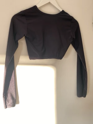 Svart croppad långärmad topp - En stilren svart croppad topp med långa ärmar och rund halsringning. Materialet är som badkläder. Perfekt att matcha med höga jeans eller kjol för en trendig look. Tunt och stretchigt material som sitter snyggt på kroppen.