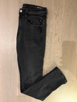 Replay Anbass grå jeans - Snygga mörkgrå jeans från Replay i modellen ”anbass”! Jeansen är i storlek W31/L32. Säljs extra billigt på grund av slitage vid Replay loggan på ena framfickan, som visas på sista bilden. Priset är diskuterbart, kontakta mig för alla frågor och funderingar! ✅🤝