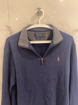 Blå halvzip från Polo Ralph Lauren - Mörkblå långärmad tröja från Polo Ralph Lauren med halvzip och kontrasterande grå krage. Broderad logga i gult på bröstet. Perfekt för lager-på-lager och snygg till jeans eller chinos. (Priset kan diskuteras)