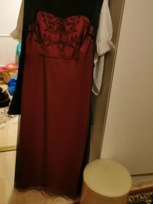 Vinröd långklänning med spetsdetaljer - Elegant vinröd långklänning med svart mesh och broderade spetsdetaljer upptill. Klänningen har en figurnära passform och transparent övre del som ger en snygg kontrast. Perfekt för dig som vill sticka ut med en unik och stilren look.