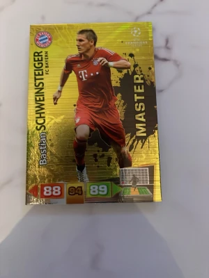 Guldfärgat fotbollssamlarkort Bayern - Samlarkort med guldfärgad bakgrund och motiv av en spelare från FC Bayern München. Kortet har texten 'MASTER' och spelarens namn samt olika poängvärden. Perfekt för dig som gillar fotboll och samlarkort.