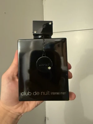 Club de Nuit Intense Man Edp 200ML parfym - Club de Nuit Intense Man från Armaf är en elegant herrparfym i en svart, fyrkantig flaska med metallisk finish och detaljer som en kedja och blanka nitar på korken. Flaskan har en modern och stilren design med silverfärgad text.