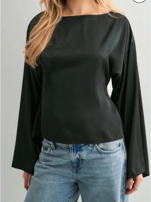 Svart långärmad topp med knyt - Trendig svart topp med lång ärm. Toppen har öppen rygg med snygg knytning baktill. Aldrig använd och har prislappen kvar. Jag har storlek vanligtvis storlek S och den passar mig bra