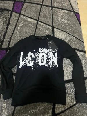 Svart sweatshirt Dsquared2 ICON - Cool svart sweatshirt från Dsquared2 med stor vit 'ICON'-print framtill och splattereffekt. Tröjan har rund hals, långa ärmar och ribbade muddar vid ärmslut och nederkant. Perfekt för en streetwear-look.