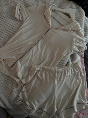 Intimissimi Beige pyjamasset med kortärmad skjorta - Mjuk och skön pyjamas i beige med kortärmad skjorta och matchande shorts. Skjortan har knäppning framtill och krage, shortsen har resår i midjan. Perfekt för mysiga hemmakvällar.