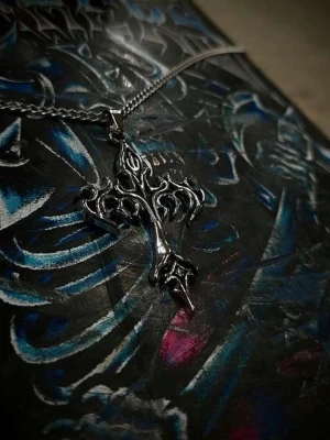 Silvrigt korshalsband med tribaldesign - Säljer ett halsband med ett stort korsformat hänge i silvrig metall. Hänget har en detaljerad tribalinspirerad design med spetsiga former och coola detaljer. Kedjan är också i silverfärgad metall och har en klassisk länkstil. Perfekt för dig som gillar alternativ stil eller vill sticka ut.