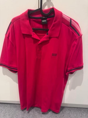Röd pikétröja från HUGO BOSS XL - Snygg röd pikétröja från HUGO BOSS med klassisk krage och knappar framtill. Nyskick!!