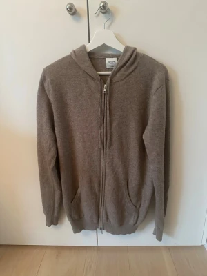 Beige zip hoodie john henric - Säljer en beige hoodie från John henric i 100% kashmir. Den har dragkedja framtill, två fickor och en klassisk huva. Perfekt för dig som gillar en enkel och stilren look med skönt material