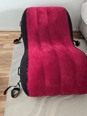 Uppblåsbar röd lounge-stol med pump - Säljer en uppblåsbar lounge-stol i röd och svart färg med ergonomisk form. Tillverkad i mjuk velour-liknande plastmaterial. Flera handtag och remmar på sidorna. Elektrisk pump medföljer för enkel uppblåsning. 