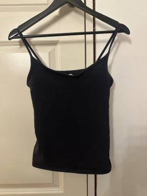 Svart linnetopp från Cubus - En marinblå, enkel och stilren linnetopp från Cubus med smala axelband. Perfekt att matcha med jeans eller kjol för en clean look. Toppen är i mjukt material och har en tight passform.