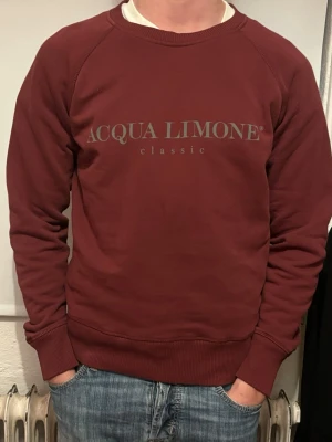 Vinröd sweatshirt Acqua Limone - Vinröd sweatshirt från Acqua Limone med tryck på bröstet och stort citrongult tryck på ryggen. Klassisk rund halsringning och ribbade muddar vid ärmslut och nederkant. Perfekt för en avslappnad och trendig stil.  Ny pris 2000kr, vårt pris 299kr✅