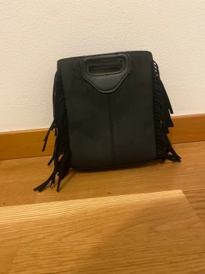 Svart handväska med fransar - 💕Kan tänka mig att gå ner i pris💕 Super snygg väska med fransar,man kan hålla i den eller ha ett band runt så de blir en axelväska.Den har fått en liten skada på ena sidan. 