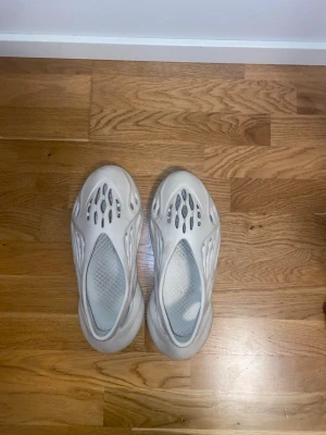 Adidas Yeezy Foam Runner sand  - Säljer ett par Adidas Yeezy Foam Runner i beige färg. Skorna har en futuristisk design med många hål och rundad form, tillverkade i syntetmaterial. Perfekt för dig som gillar streetwear och vill sticka ut med en unik look.