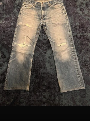 Levi's 507 blå jeans med slitningar - Säljer ett par Levi's 507 jeans i klassisk blå tvätt med coola slitningar och distressed detaljer på benen. Bootcut fit och skön fade