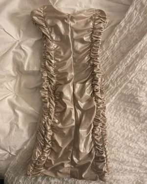 Champagnefärgad kort klänning Bershka - Supersnygg kort klänning från Bershka i glansigt champagnefärgat tyg. Klänningen har åtsittande passform, rynkade detaljer längs sidorna och dragkedja i ryggen. Perfekt för dig som vill sticka ut med en trendig look.