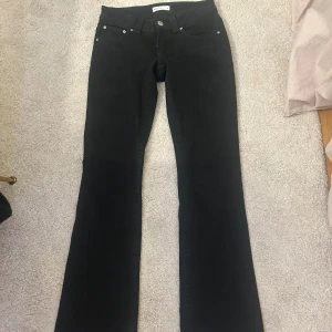 Svarta bootcut jeans från Gina Tricot - Svarta jeans från Gina Tricot, modell Perfect Jeans, med bootcut-ben och klassisk femficksdesign. Snygga silverfärgade knappar på bakfickorna och fram. Jeansen har normal passform och är tillverkade i mjukt jeansmaterial.