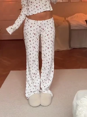 Nelly pyjamas  - Säljer en vit långärmad tröja med små söta mönster i olika färger. Tröjan har en avslappnad passform och är tillverkad i mjuk bomull, perfekt för chill dagar hemma. Den har en croppad längd och matchar med pyjamasbyxor för en mysig look. Finns en oboy fläck som ej går bort, 