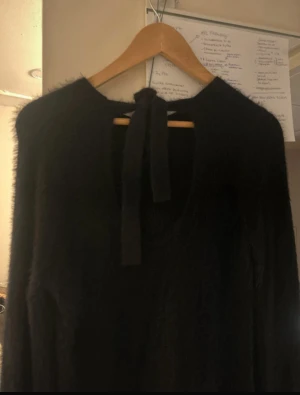 Svart fluffig stickad tröja KappAhl - Mysig svart stickad tröja från KappAhl med fluffig känsla. Tröjan har lång ärm och en snygg knyt-detalj i nacken som ger en extra touch. Perfekt för dig som gillar en enkel men ändå trendig look.