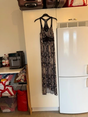 Lång boho-klänning med spetsdetaljer - Säljer en lång bohemisk klänning med svart och beige paisleymönster, tunna axelband och snygga virkade spetsdetaljer i ryggen och under bysten. Klänningen har v-ringning och ärmlös design, perfekt för sommarens alla äventyr. Luftigt material och flowy passform. Från märket Odd Molly. Storlek 2 som enligt deras storleksguide motsvarar en M. Mer använd, men fortfarande fint skick, 