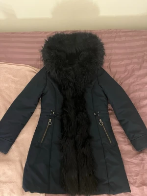 Mörkblå jacka med päls - Snygg mörkblå vinterjacka med stor fluffig fuskpäls. Jackan har långa ärmar, dragkedjor med ringdetaljer på fickorna. Perfekt för kalla dagar när du vill vara både varm och stilren. Priset går att diskutera. ❤️