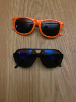 Hornbach orange solglasögon - Säljer ett par orangea solglasögon från Hornbach med klassisk wayfarer-form och svarta linser. Plastbågar med tryckt Hornbach-logga på sidan. Perfekt för dig som vill sticka ut med färg och enkel stil. Inga repor eller större sprickor i dom