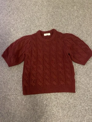 Vinröd stickad tröja  - Vinröd stickad tröja från Samsa Collection i storlek XS. Tröjan har korta puffärmar och ett mönster på hela tröjan. Har aldrig använt! 