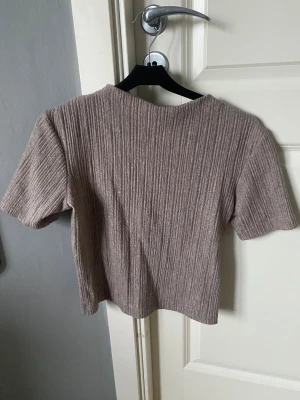 Beige ribbad topp med kort ärm - Säljer en beige ribbad topp med korta ärmar och rund hals. Toppen har en croppad passform och är gjord i ett mjukt, stretchigt material som känns skönt mot huden. Perfekt till jeans eller kjol för en chill och enkel look.